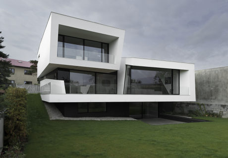 A modern, two-story residential building with a clean, minimalist exterior design featuring large glass windows and a cantilevered second floor.