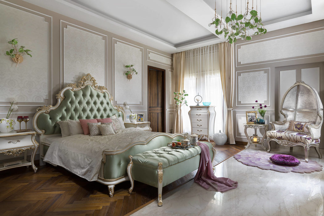Ornate, lavish bedroom with tufted green headboard, gilded decor, and delicate chandelier.