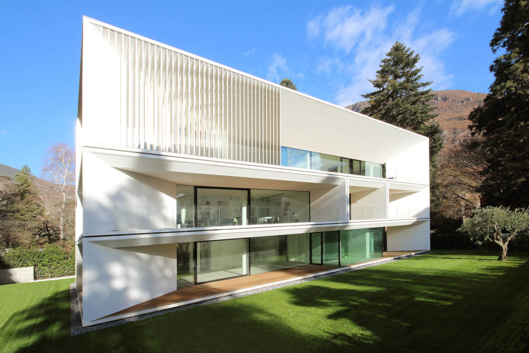 A striking modern home with clean lines, expansive glass walls, and a lush green lawn.