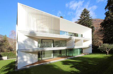 A striking modern home with clean lines, expansive glass walls, and a lush green lawn.