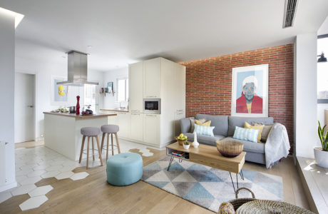 Modern open-plan kitchen-living space with white cabinets, brick wall, and eclectic decor.