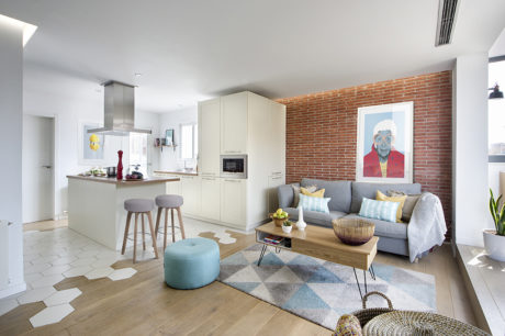 Modern open-plan kitchen-living space with white cabinets, brick wall, and eclectic decor.