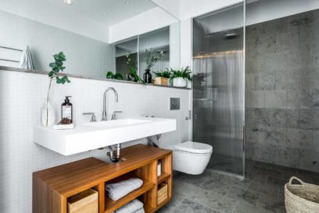 Minimalist bathroom design featuring a white sink, wooden vanity, and gray tile walls.