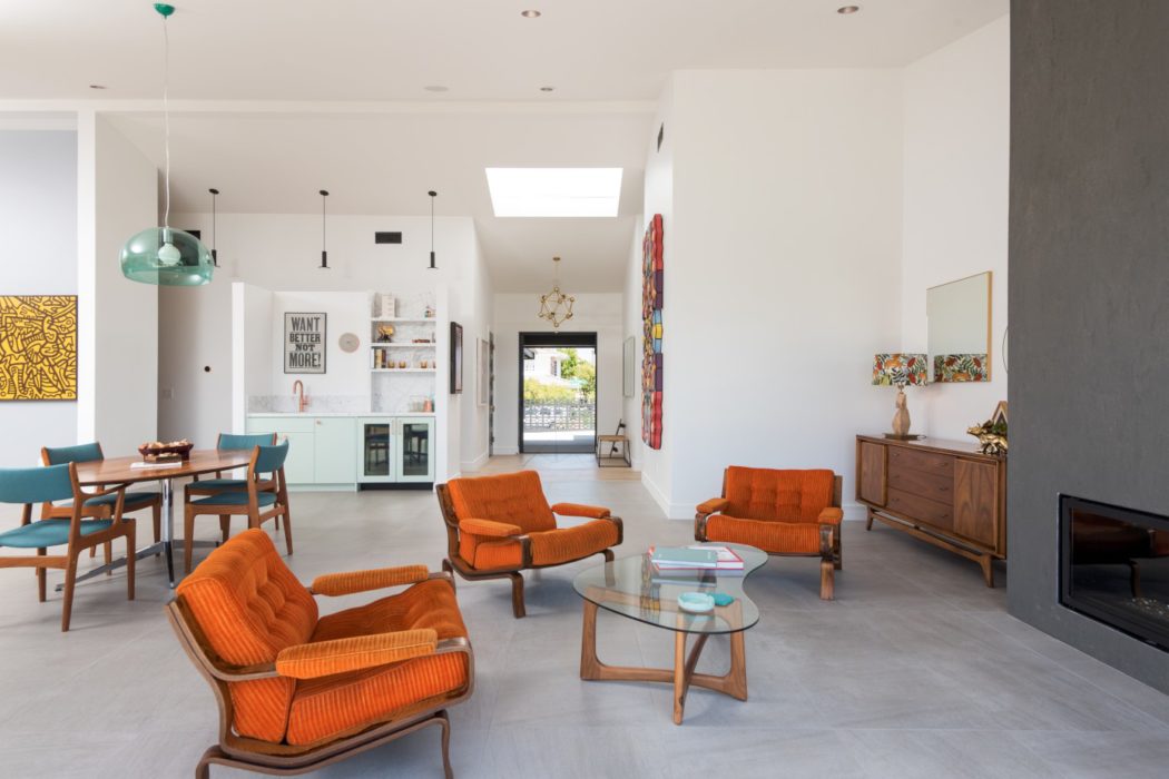 This bright, modern open-concept living space features vibrant orange furniture, exposed beams, and natural lighting.