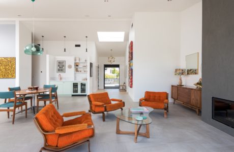 This bright, modern open-concept living space features vibrant orange furniture, exposed beams, and natural lighting.