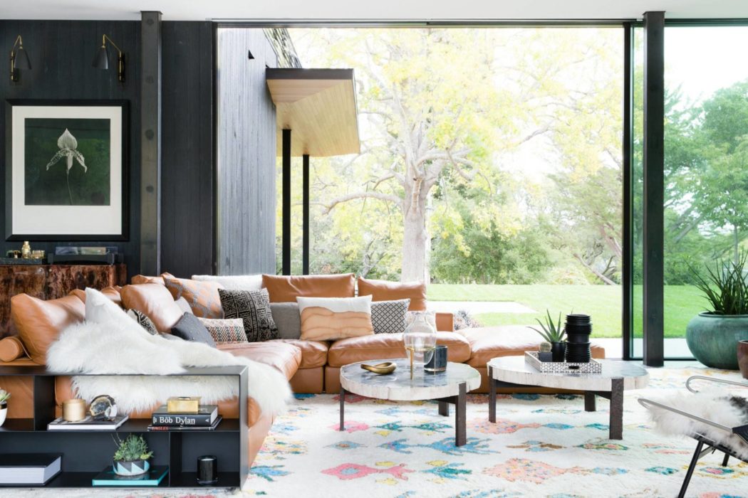 A chic modern living room with glass walls overlooking a lush outdoor scene.
