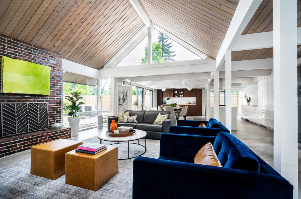 A modern, open-concept living space with vaulted wooden ceilings, exposed beams, and a mix of contemporary and rustic furnishings.