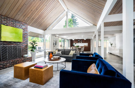 A modern, open-concept living space with vaulted wooden ceilings, exposed beams, and a mix of contemporary and rustic furnishings.