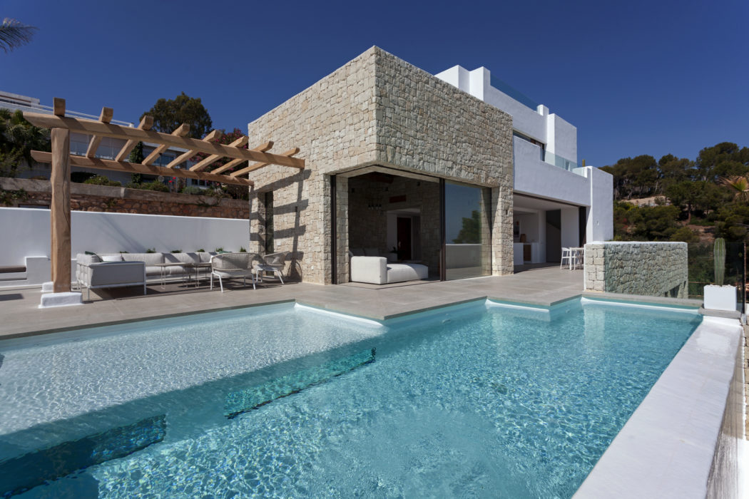 Modern Mediterranean villa with stone facade, pool, and lounge area.