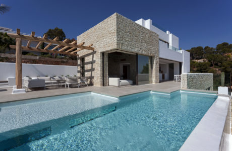 Modern Mediterranean villa with stone facade, pool, and lounge area.