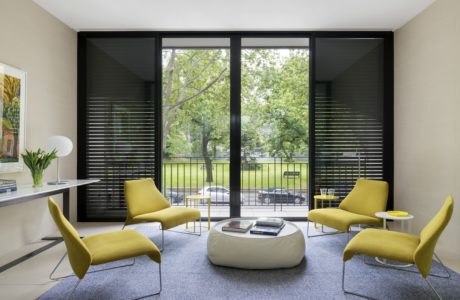 Modern living room with sleek black window frames, bright yellow chairs, and a circular coffee table.