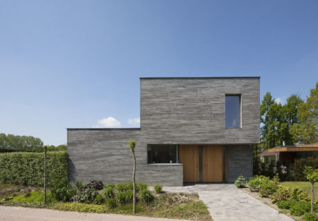 A modern, minimalist two-story residence with a wooden front door and a paved walkway.