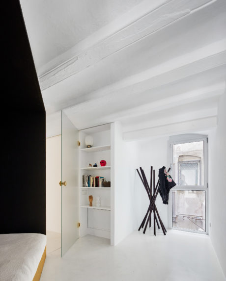 A cozy, white-walled room with a bookshelf and decorative black poles near a window.