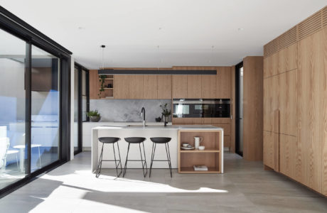 Minimalist kitchen design with wood cabinetry, white island, and large sliding glass doors.