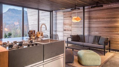 Rustic cabin interior with modern kitchen, large windows, and cozy living area.