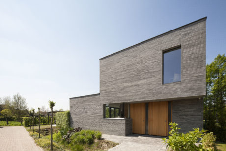 Modern residential building with clean lines, wood and brick facade, large windows, and landscaped yard.