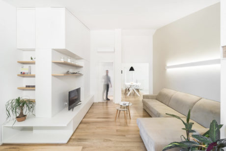 Minimalist living room with wooden floors, open shelving, and neutral furniture.