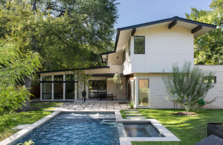 A modern, two-story home with clean lines, large windows, and a swimming pool in a lush, wooded setting.