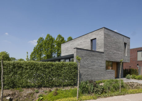 Contemporary brick home surrounded by lush greenery and landscaping.