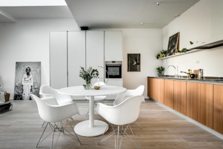 Minimalist kitchen and dining area with white chairs, wooden cabinets, and natural lighting.