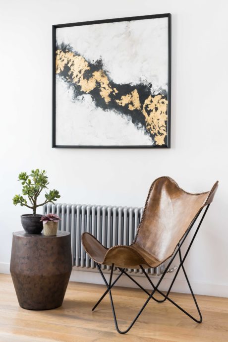 Sleek, modern design with leather chair, potted plants, and abstract artwork against white wall.