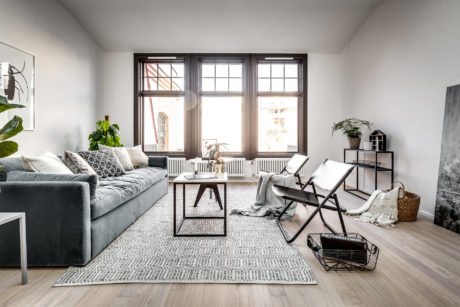 A cozy living room with large windows, a gray sofa, and a rustic wooden table.