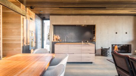 Minimalist kitchen with sleek wood cabinets, gray tile backsplash, and a cozy fireplace.