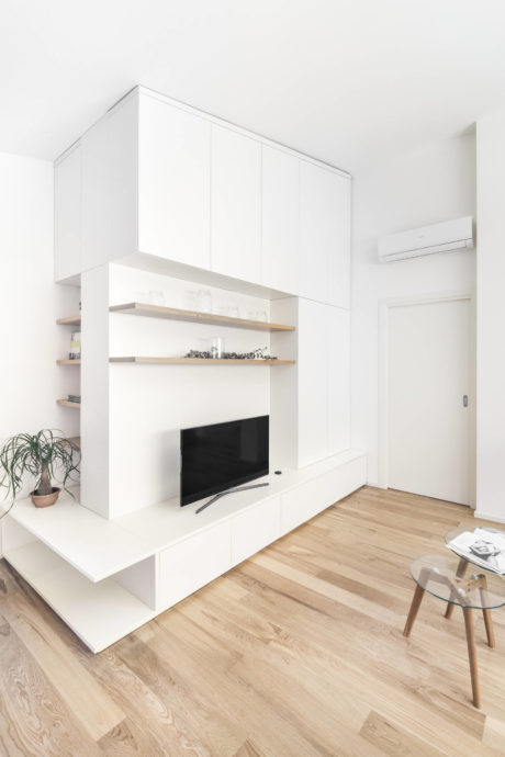 Minimalist living room with white built-in cabinetry, floating shelves, and hardwood flooring.