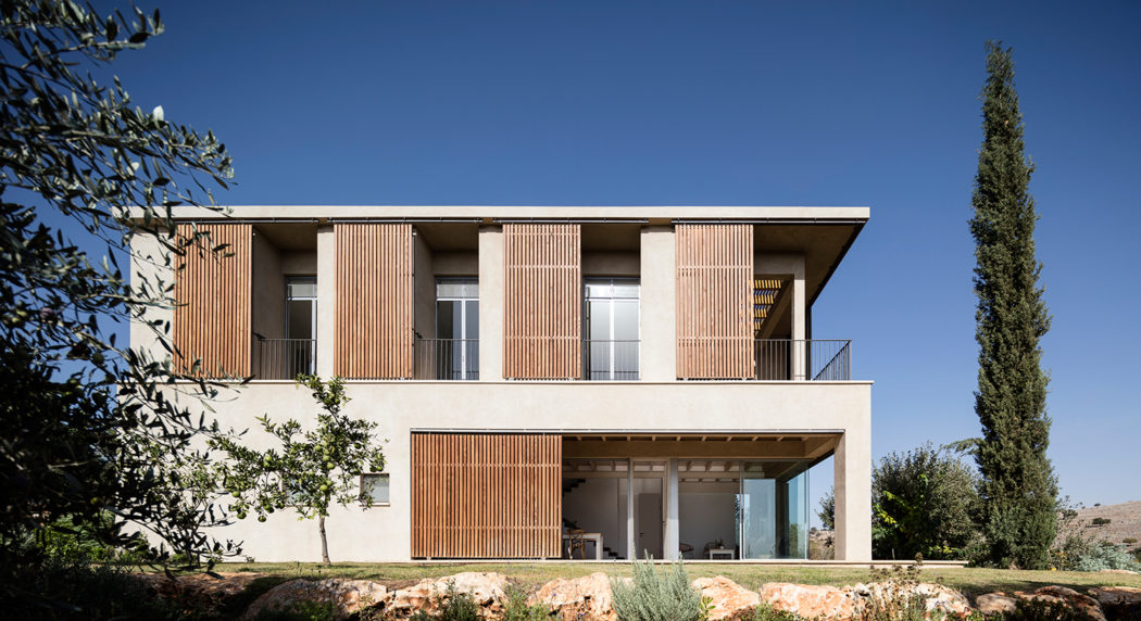 Modern two-story house with wooden slat facade, balconies, and large windows overlooking lush vegetation.