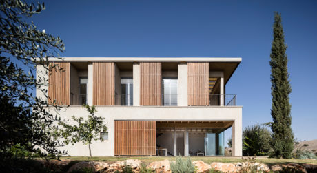 Modern two-story house with wooden slat facade, balconies, and large windows overlooking lush vegetation.