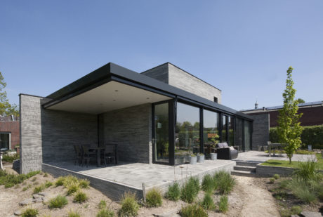 A modern, minimalist home with sleek black exterior, large glass panels, and a spacious terrace.