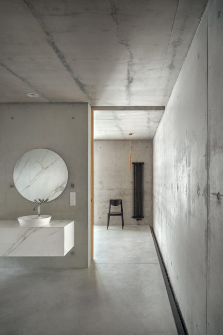 Minimalist bathroom with a round mirror and a black chair in the background.