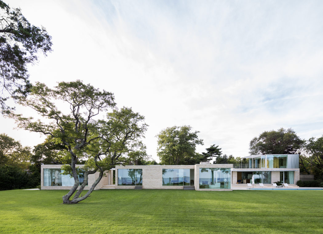 A modern, glass-walled residential structure, with a vast green lawn and mature trees.