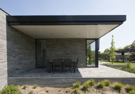 Modern exterior with sleek black overhang, stone walls, and dining area on patio.