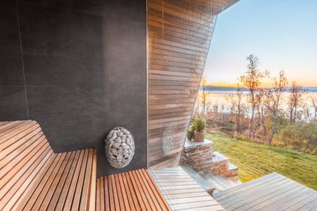 Modern wooden and concrete sauna with scenic lake view and nature through glass wall.