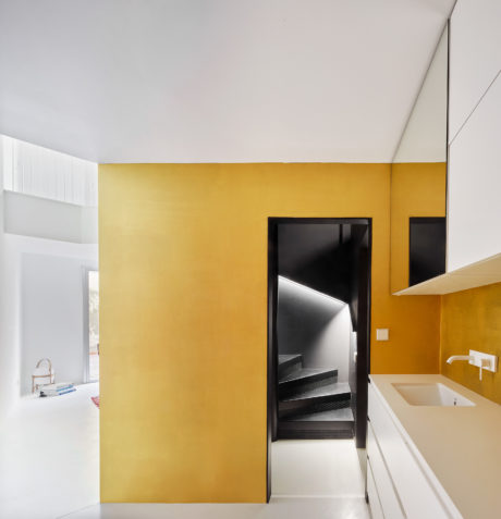 A modern interior with stark white walls, vibrant yellow accents, and a sleek black staircase leading to a loft.