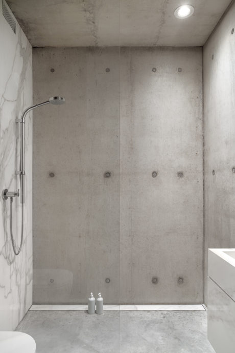 A minimalist bathroom with concrete walls, a shower, and a simple two-bottle display.