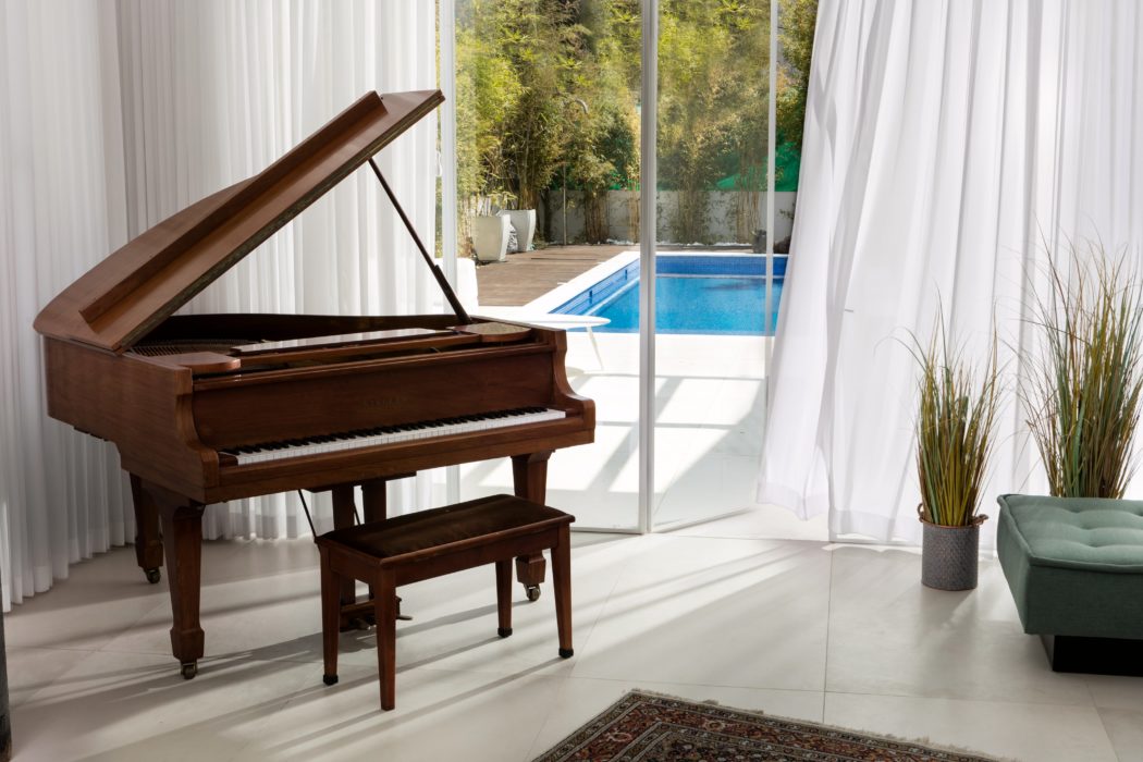 A grand piano sits in a bright, modern living room with floor-to-ceiling windows overlooking a backyard pool.