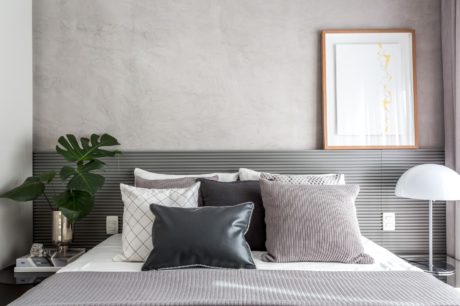 A minimalist bedroom with a patterned headboard, potted plant, and framed artwork on the wall.