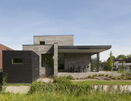 A modern, minimalist house with sleek, wood-paneled exterior and covered patio area.
