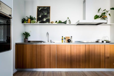 Sleek, modern kitchen with wood-paneled cabinets, floating shelves, and potted plants.