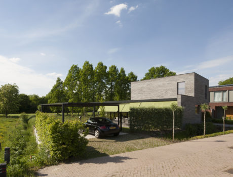 Contemporary building with a flat roof, glass facade, and covered parking area surrounded by trees.