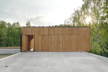 Expansive wooden facade with contrasting concrete platform and surrounding greenery.