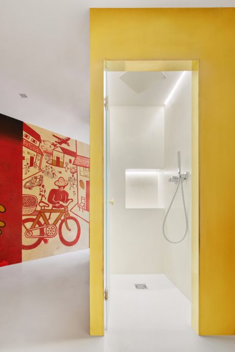 A modern bathroom with a bright yellow wall and a red wall mural featuring cartoon figures.