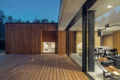 A modern, wooden cabin with a deck and large glass windows overlooking the forest.