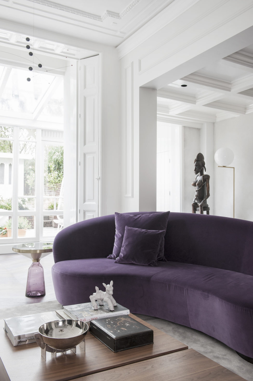 Bright, modern interior featuring a plush purple couch, ornate decor, and large windows.