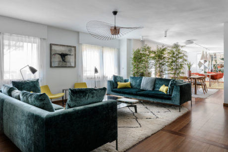 Spacious modern living room with plush emerald sofas, elegant lighting, and lush greenery.