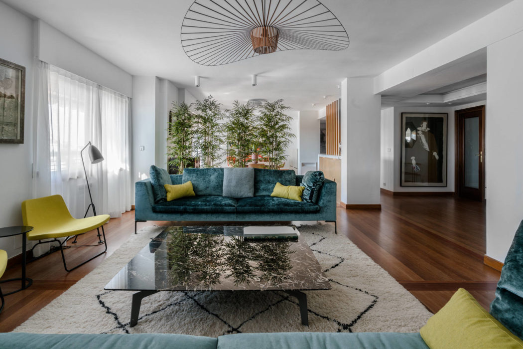 Spacious modern living room with plush teal sofa, glass coffee table, and statement lighting.