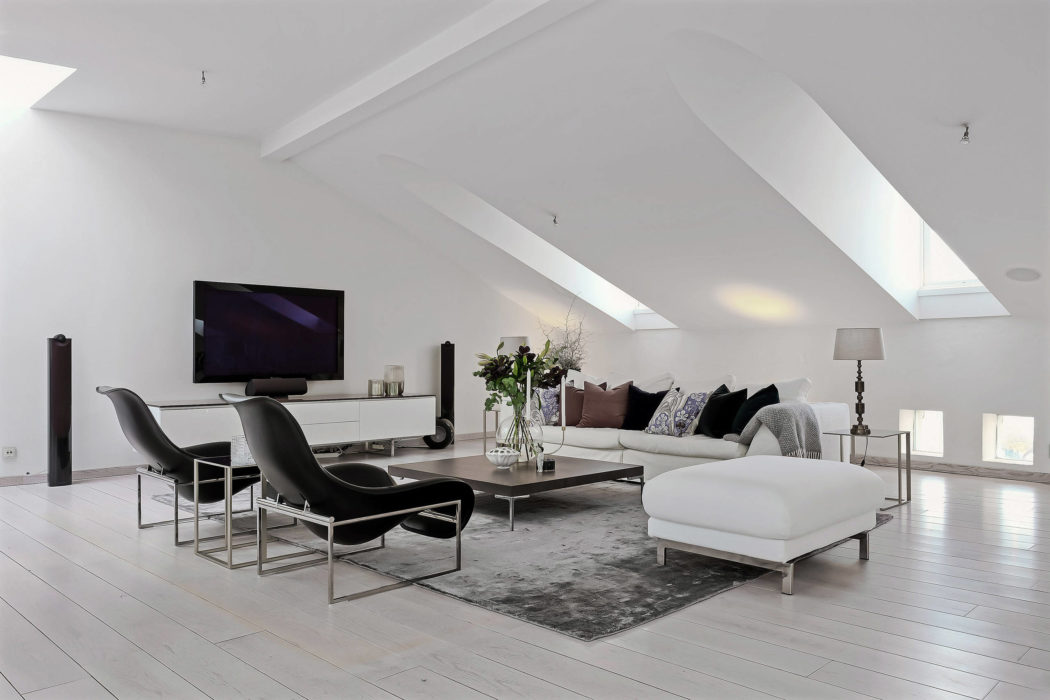Modern, bright living room with sleek furniture, exposed beams, and TV on wall.