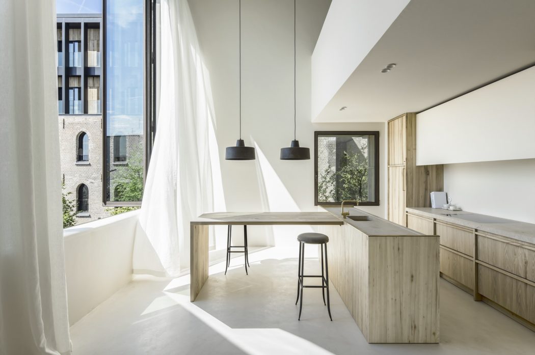 Modern kitchen with minimalist wood and white decor, pendant lights, and large windows overlooking the city.